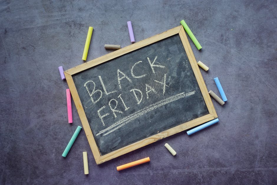 A collection of various promotional sale signs and labels displayed on a wooden surface, including rectangular, oval, and circular shapes in shades of red, white, pink, and beige. Prominent signs advertise discounts such as 'Black Friday Sale' with 25% off everything, '50% Off Super Sale', and 'Extra 40% Off Final Sales Styles'. The signs feature bold typography, decorative borders, and contrasting colors to attract attention. The arrangement includes both small individual labels and larger posters, with some overlapping slightly, creating a cluttered but organized display typical for retail promotional displays. The wooden background provides a warm, textured surface that contrasts with the bright and pastel-colored signs, emphasizing their visibility. This scene appears to be part of a sales display for a store or market, showcasing different promotional offers designed to attract customers. The overall setup suggests a focus on reducing stock or promoting seasonal discounts, aligning with practices around private, independent sales, or clearance events often associated with waste reduction in retail environments, indirectly supporting reuse and repurposing efforts. The lighting is even and natural, enhancing textual clarity and detail, making all signs easily readable for accessibility purposes.
